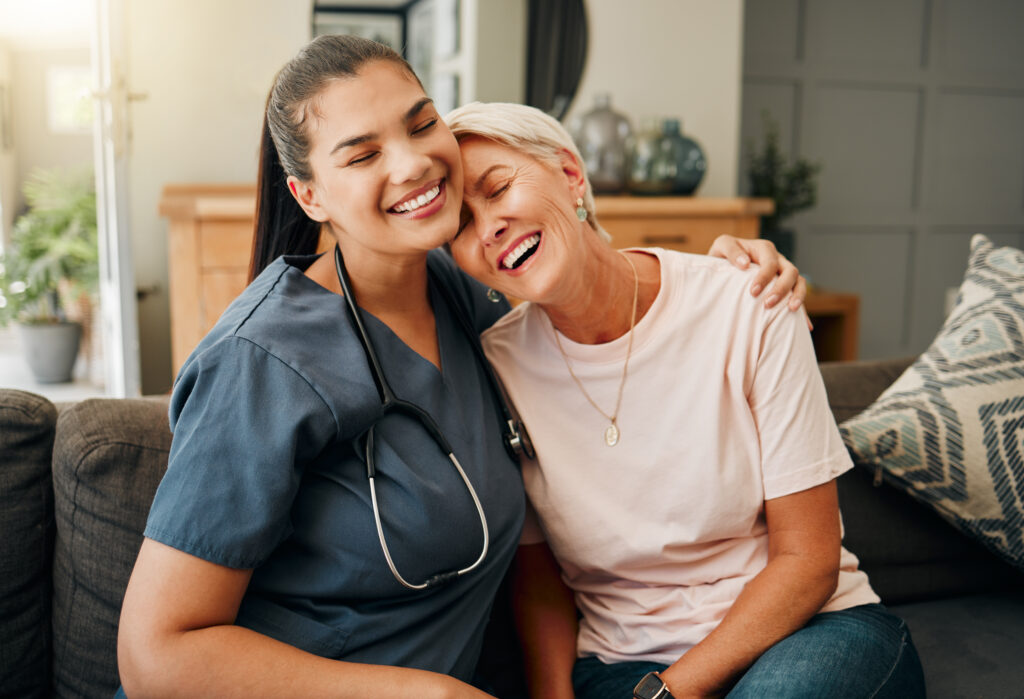 Senior woman, hug or medical caregiver in house living room in comfort trust, support or security bond. Smile, happy or laughing nursing home retirement elderly and healthcare Brazilian nurse or help.